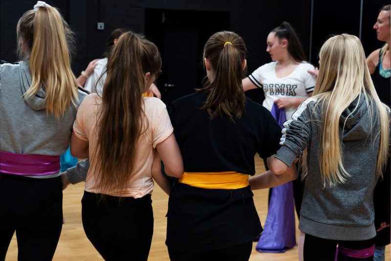 A group of students stand arm-in-arm during a workshop activity.