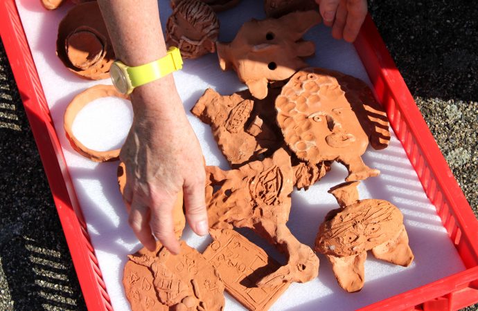 A hand picks up the ceramic objects, made as part of Alison Cooke's 'Future Archaeology of Ebbsfleet', from a red crate lined with padding..